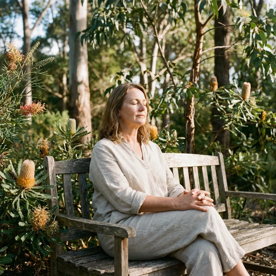 Woman resting with her eyes closed on a weathered timber bench among banksia and eucalypts