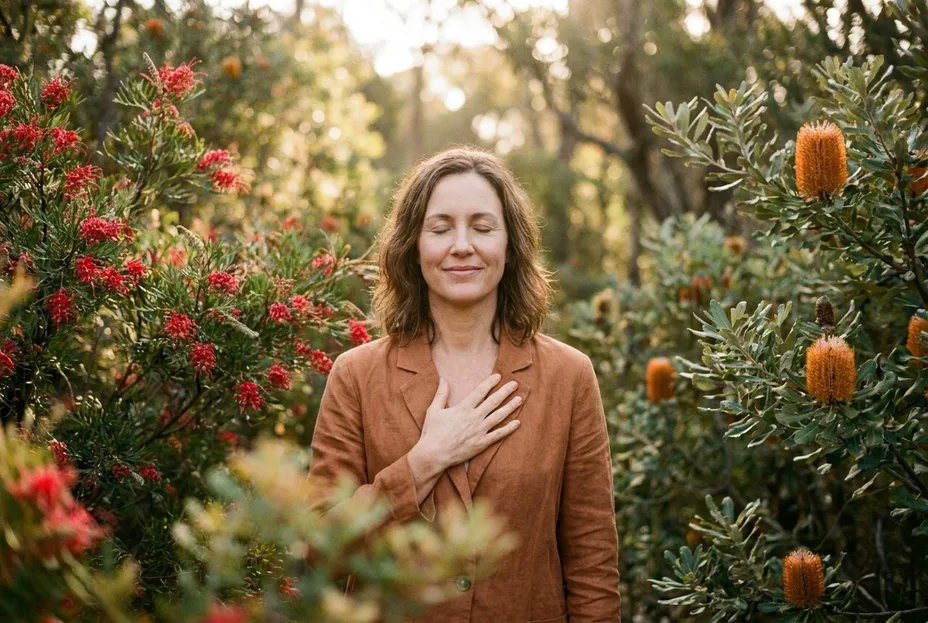 Woman standing among flowering grevillea and banksia with a hand on her heart during a women’s wellness session for Shellharbour